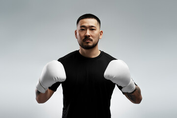 Portrait of handsome Korean man wearing white boxing gloves, standing isolated on gray background