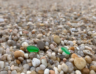 Pieces of green sea glass lying on a pebble beach. Close up, shallow depth of field.