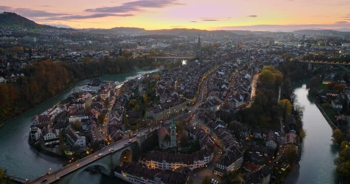 Wide establishing aerial sunset over Bern town, the capital city of Switzerland with colorful twilight romantic sky. Drone fly over Aare river Swiss historic cityscape traveling landmark in autumn.