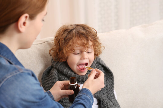 Mother giving cough syrup to her son on sofa indoors