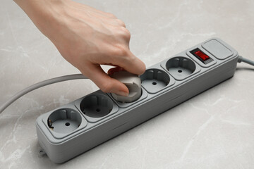 Woman putting plug into extension cord at grey marble table, closeup. Electrician's equipment