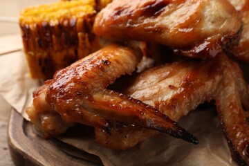 Delicious baked chicken wings and grilled corn served on wooden table, closeup