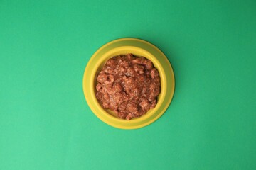 Wet pet food in feeding bowl on green background, top view