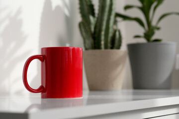 Red ceramic mug on white table indoors. Mockup for design