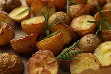 Tasty baked potato and aromatic rosemary on parchment paper, closeup
