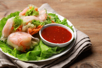 Tasty spring rolls served with lettuce and sauce on wooden table, closeup