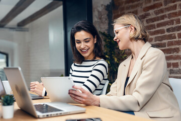 Fototapeta premium Two beautiful designer women working with laptop while choosing materials in digital tablet in the modern office.