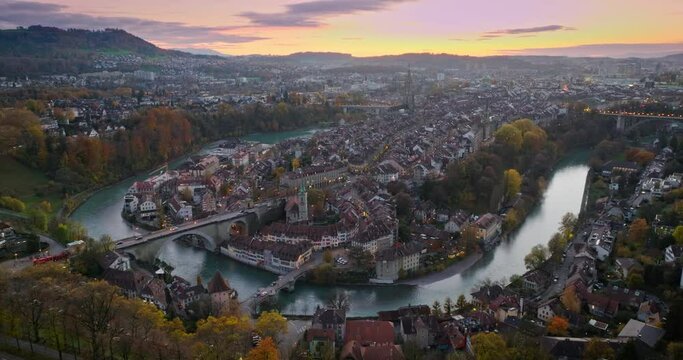 Wide establishing aerial sunset over Bern town, the capital city of Switzerland with colorful twilight romantic sky. Drone fly over Aare river Swiss historic cityscape traveling landmark in autumn.