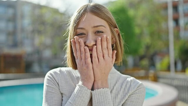 Young blonde woman standing with surprise expression at park