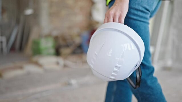 Young blonde woman builder holding hardhat walking at construction site