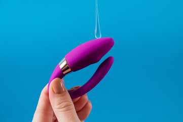 A woman holds a curved sex toy in lubrication on a blue background. Vaginally clitoral vibrator.
