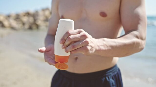 Young hispanic man tourist applying sunscreen on arm at seaside