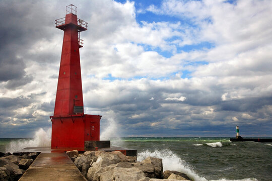 Red lighthouse with waves crashing in harbor on a windy overcast day in Muskegon, on Lake Michigan USA