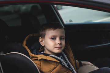 Preschool cute 6 years old boy sitting in safety car seat  and looking sadly at the camera
