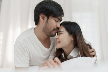 Obraz na płótnie Canvas Asian Romantic couple in bed enjoying sensual foreplay Happy sensual young couple lying in bed together. Beautiful loving couple kissing in bed.