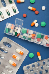 Daily pill box with medications and nutritional supplements on blue background. Space for text