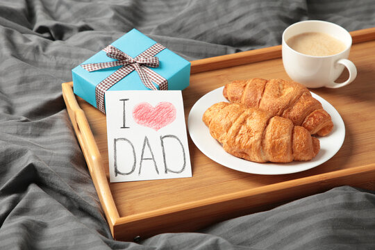 Father's day concept with gift, card and breakfast on tray. Breakfast for dad with croissant and coffee.
