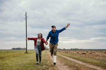 Loving diverse working couple running with arms spread on the countryside field.