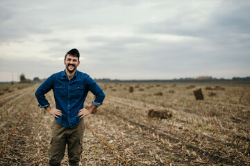 Naklejka na ściany i meble Portrait of a smiling male farmer in working outfit standing in his agricultural land and welcoming and showing his property, Copy space
