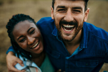 Close up portrait of a diverse couple looking and smiling towards the camera while spending a day outdoors. Lifestyle concept