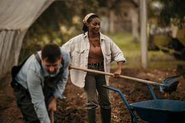 Two diverse dedicated agricultural workers using a shovel and a wheelbarrow and taking care of the...