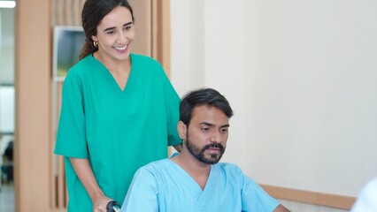 Fototapeta premium Young woman nurse pushing wheelchair of indian male patient going to treatment room at hospital
