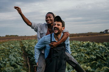 Smiling embraced diverse working couple having a piggyback ride and fun while spending time on their farm together.