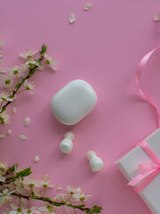 White wireless headphones on pink background with cherry flowers, gift box and copy space. Womens, Valentines and Mothers Day gift. Concept of music and elegance. Buying birthday gifts. 
