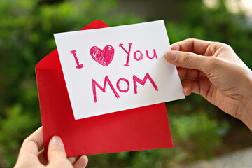 Woman hands holding a Mother's Day greeting card with red envelope, I Love You Mom message on the card.