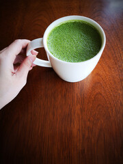Hand holding a cup of green tea with milk or hot matcha latte on the wooden table in cafe with copy space    