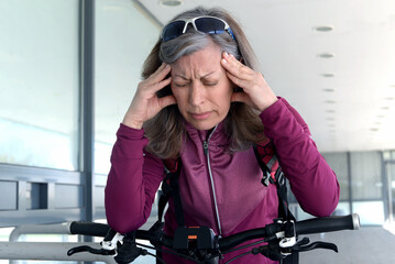 A middle-aged woman is riding a bicycle and has stopped because she has a headache