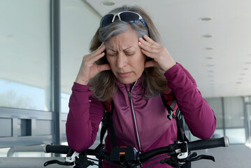A middle-aged woman is riding a bicycle and has stopped because she has a headache