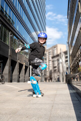 a boy in a protective helmet rides a blue city curezer, a plastic skateboard in the spring through the urban streets of the city	