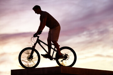 Obraz premium Silhouette, sunset and cycling with man on bicycle for sports, adventure and fitness. Action, exercise and health with male cyclist riding on bmx bike for journey, urban or carbon neutral with mockup