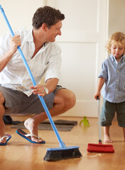 Man is cleaning with boy child, sweeping with broom and help with mess on floor while at home...