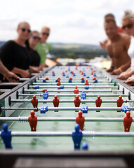 Naklejka na ściany i meble Friends playing with a foosball at a party for competition, fun skill or sports event. Celebration, activity and group of people enjoying a football table game or match for a friendly championship.