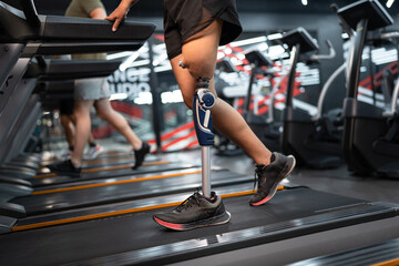 Low angle view at woman with prosthetic leg walking in treadmill at fitness gym	