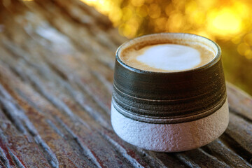 Hot latte coffee in a round mug on an old wooden table with warm light and copy space
