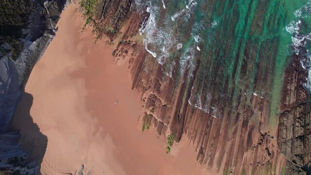 Beach shore aerial, push out topview, oceanic sea waves washing on a rocky sand coast in slow motion slomo, Playa de Tagle, Spanish coast. 