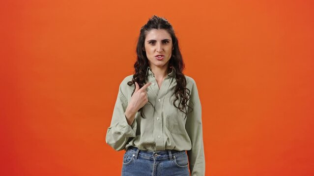 Caucasian young woman expressing denial and refusal while pointing at herself, isolated on orange