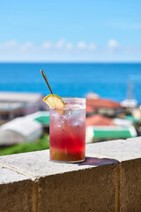 Red summer drink or cocktail with ice. Tropical fruit drink. Blue sea and blue sky, horizon background. jeju island.