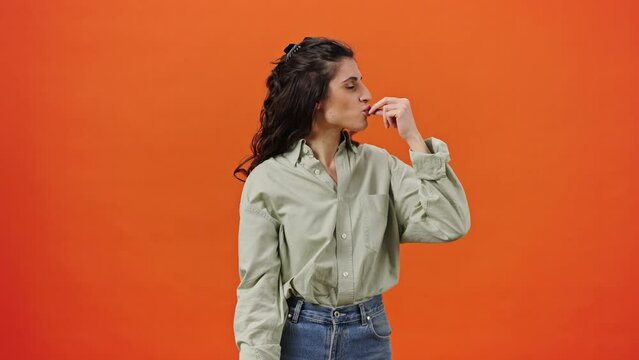 Caucasian emotional woman showing tasty gesture, kisses fingers and says bellissimo, orange backdrop