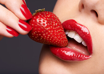 Beauty, makeup and woman with a strawberry in a studio with red nails and lipstick cosmetics. Health, wellness and closeup of a female model eating fruit for nutrition isolated by a gray background.