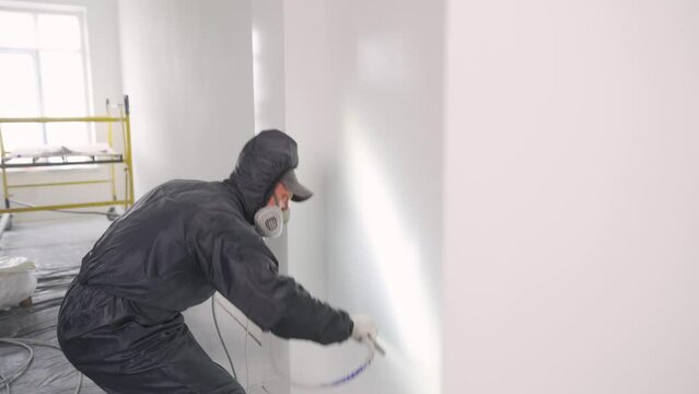 Labor, Hard work. Painter worker builder man in protective gear works. Paints with an airless spray.