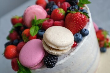 Birthday or anniversary cake with cream cheese frosting decorated with macaroons, fresh raspberries, strawberries, blackberries and blueberries. 
