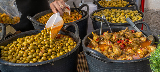 Wide selection of pickled olives and aubergines from almagro in a food stall a traditional market in the street of a village with the seller preparing and picking olives with ladle