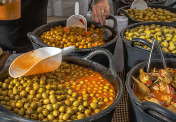 Wide selection of olives and aubergines in almagro pickle at a food stall a traditional street market in a village with the vendor preparing the order with ladle