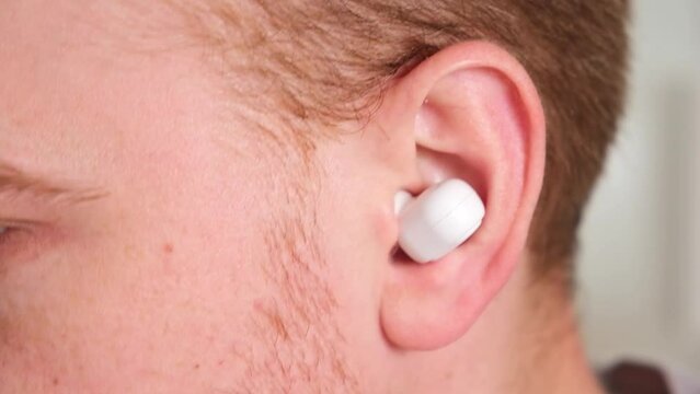 The guy pulls out of the case and inserts wireless headphones into his ears. Young man showing wireless headphones.