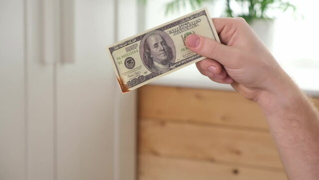 A man sets fire to 100 dollar bills. Crisis. Hand holding burning dollar bills banknotes