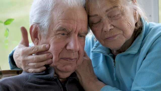 Elderly couple hugs together sitting in nursing home. Lonely people deprived of care and attention. Support and helping hand. Face with wrinkles and gray hair. Woman carefully strokes an old man head